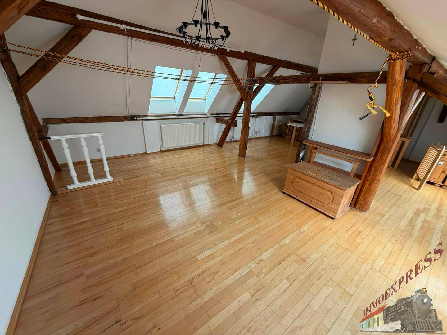 Heller Dachbodenraum mit Holzbalken, Dachfenstern und glänzendem Holzparkettboden.