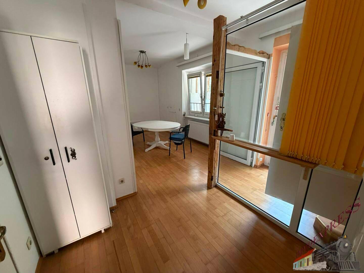 Heller Raum mit Holzfußboden, einem runden Tisch und einem großen Fenster.