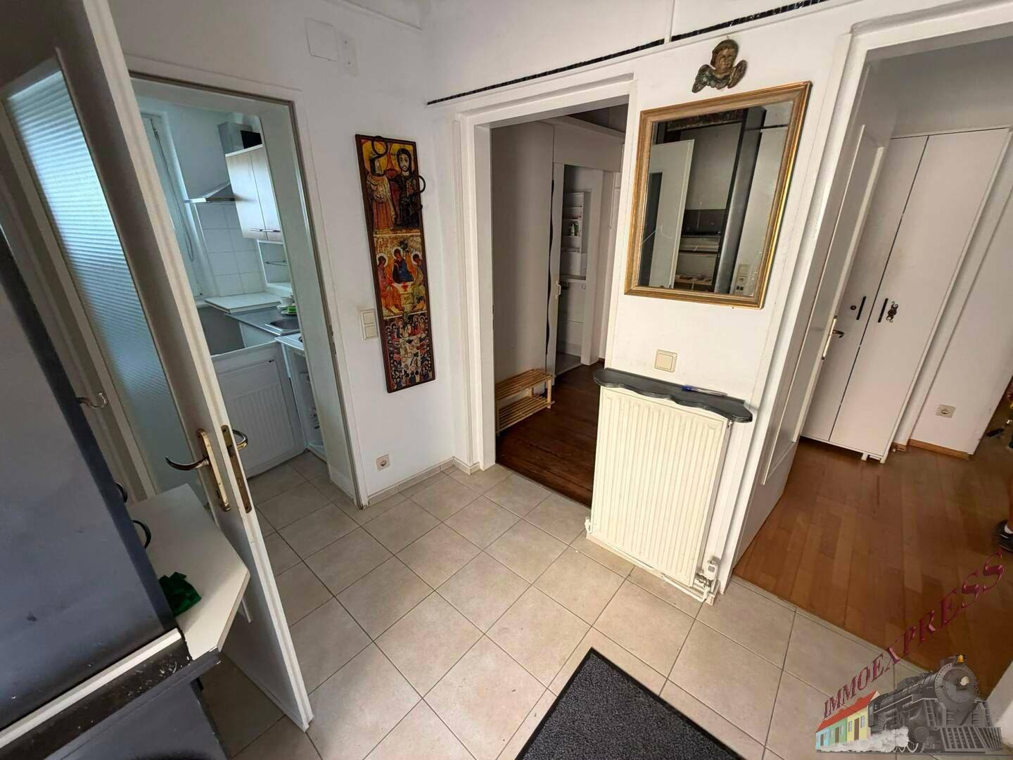 Eingangsbereich mit Fliesenboden, Zugang zu weiteren Räumen und einem Heizkörper.
