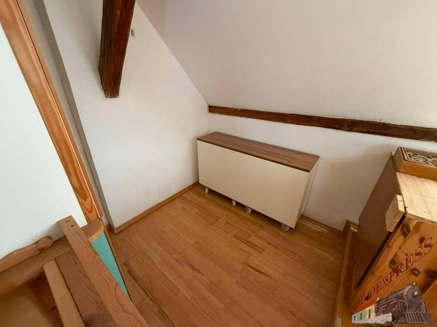 Kleiner Raum im Dachgeschoss mit schrägen Wänden, Holzbalken und Holzfußboden.