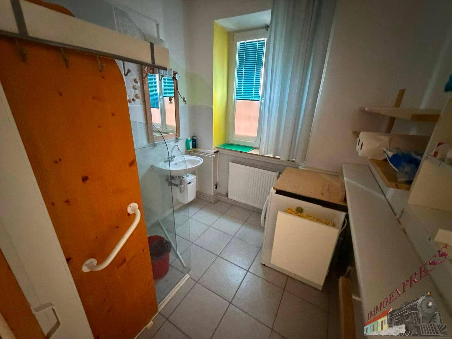 Badezimmer mit Duschkabine, Waschbecken, Fenster und Fliesenboden.