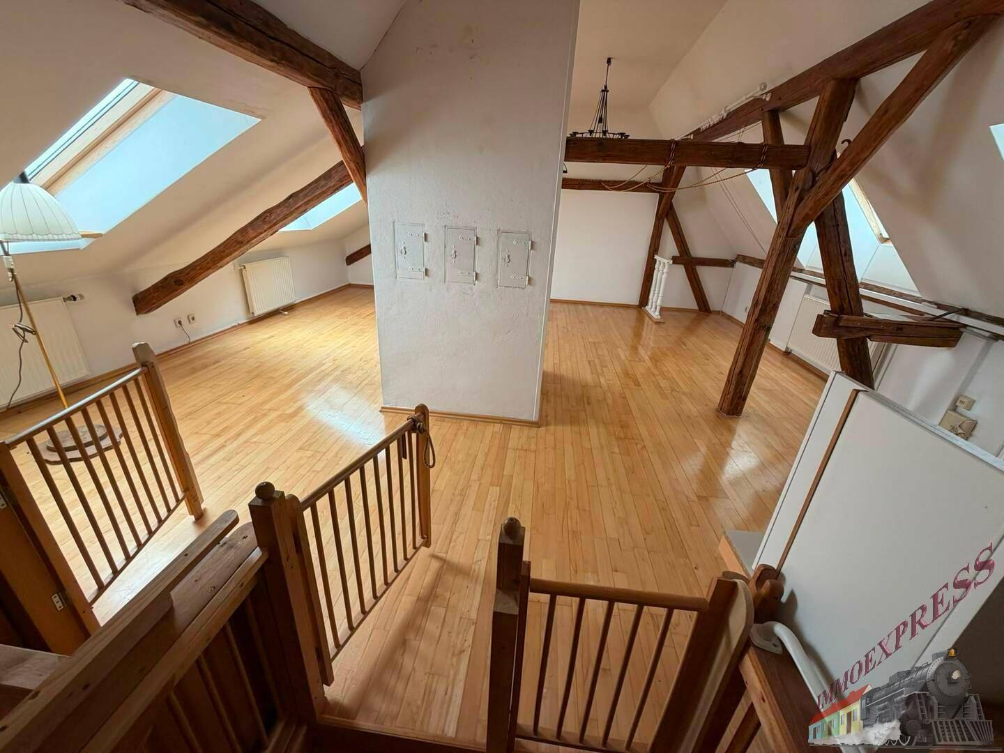 Geräumiger Dachboden mit sichtbaren Holzbalken, Dachfenstern und Holzfußboden.