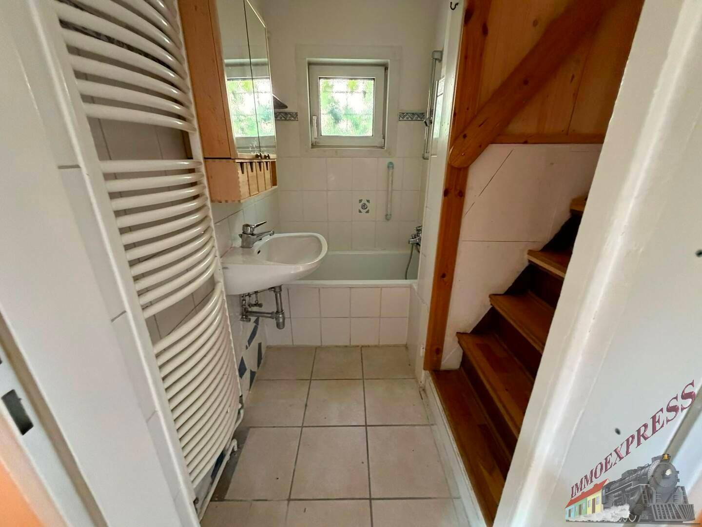 Kleines Badezimmer mit Badewanne, Waschbecken, Fliesenboden und Handtuchheizkörper.