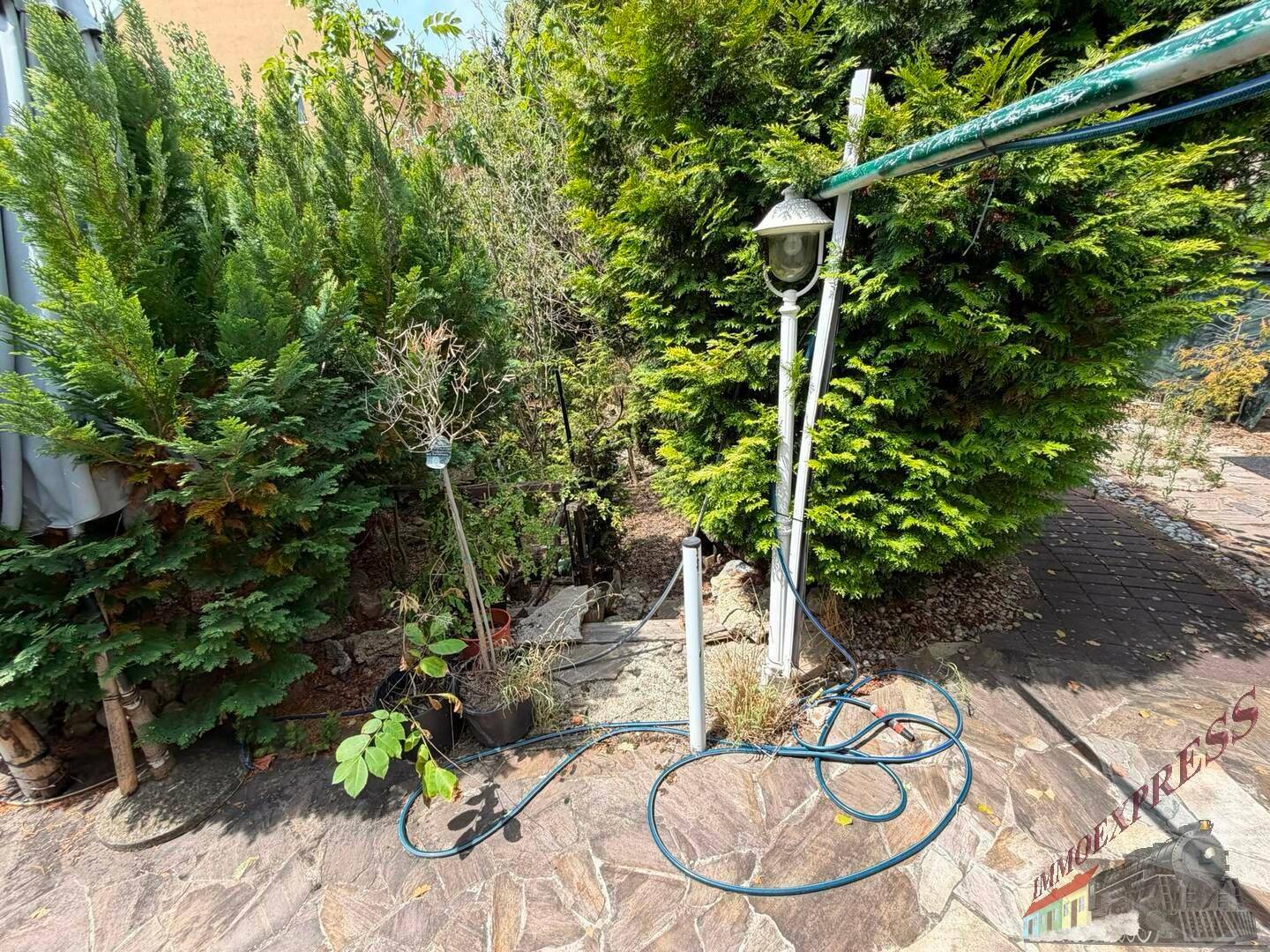 Steinplattenweg im Garten mit üppiger Bepflanzung und einer Gartenlaterne.