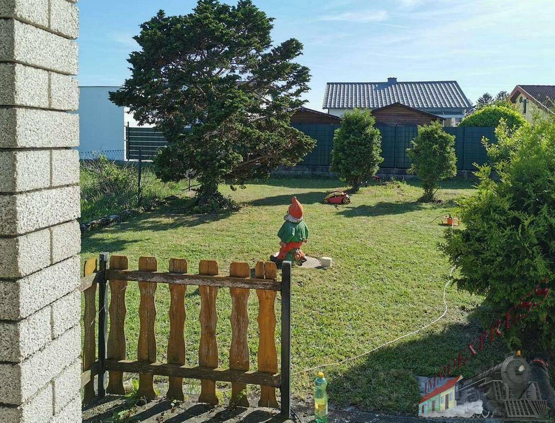 Weitläufiger Rasengarten mit einem Gartenzwerg und Blick auf weitere Häuser in der Ferne.