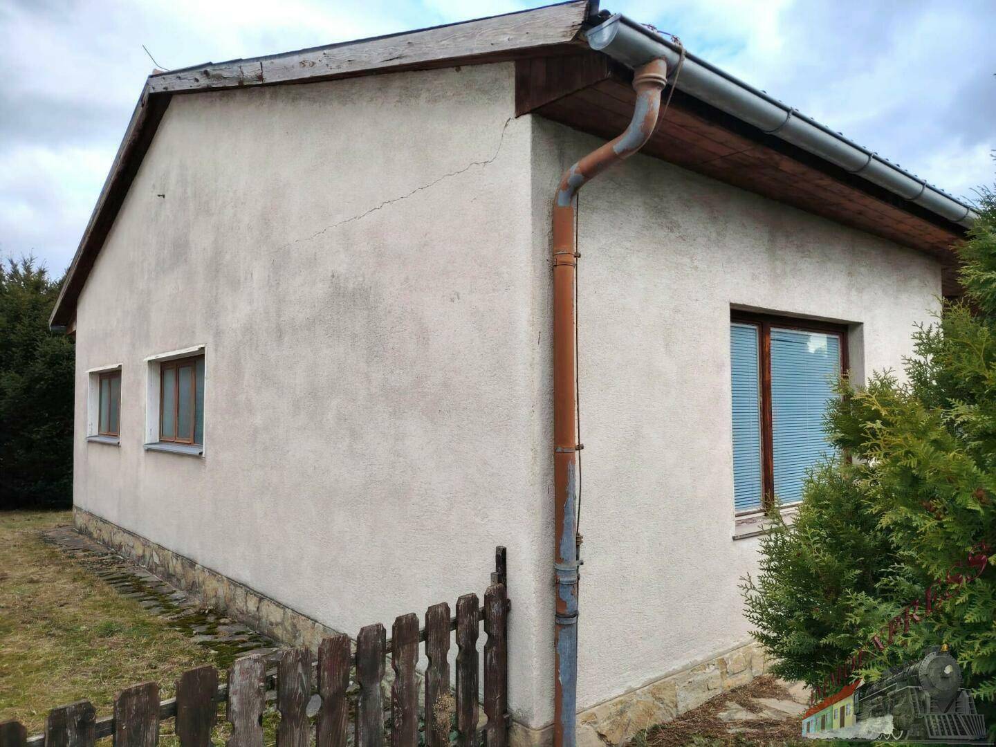 Seitenfassade des Hauses mit Putz, Fenstern und einem alten Dachrinnensystem.