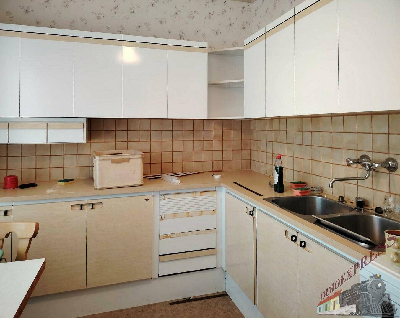 Ältere Einbauküche mit hellen Holzfronten, beigen Fliesen und Doppelspülbecken.