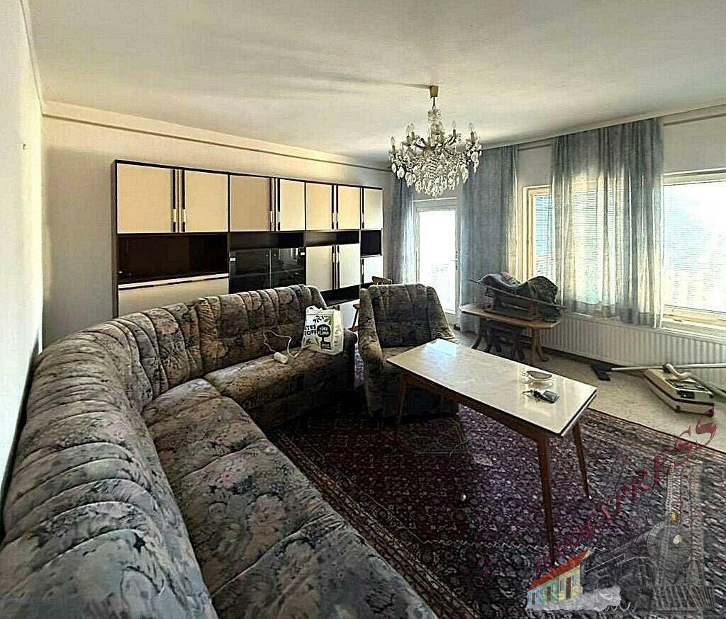 Geräumiges Wohnzimmer mit Ecksofa, Teppich, Schrankwand und Fenstern mit Jalousien.