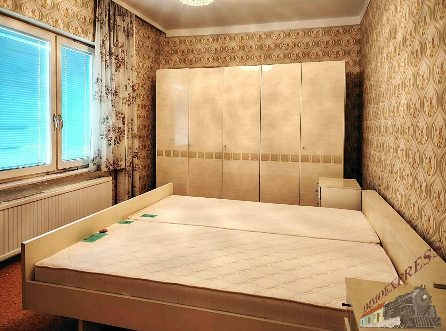 Schlafzimmer mit Doppelbett, großem Kleiderschrank und gemusterter Tapete im Retro-Stil.