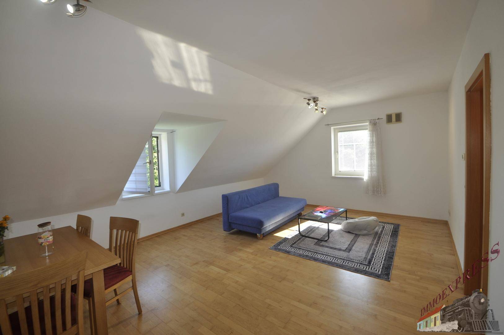 Geräumiger Wohnbereich mit gemütlichem Sofa, Holzboden und viel Tageslicht durch die Fenster.