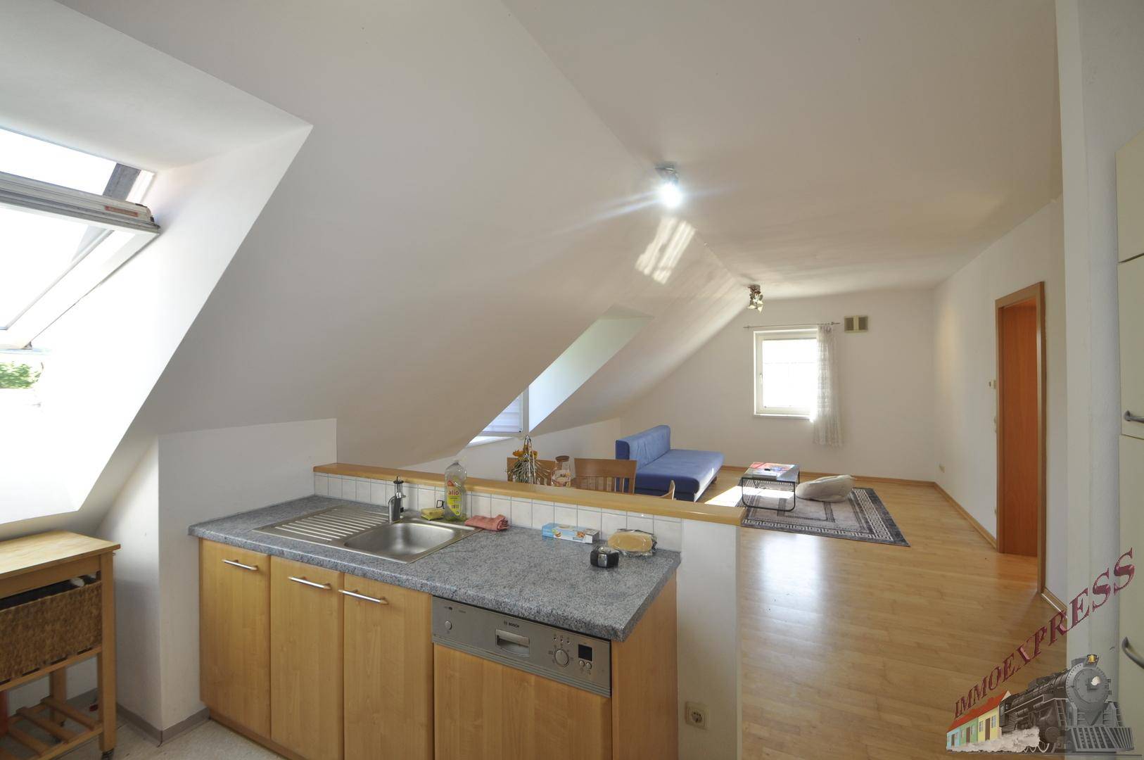 Funktionale Küche mit Arbeitsplatte und Blick auf den Wohnbereich, beleuchtet durch ein Dachfenster.