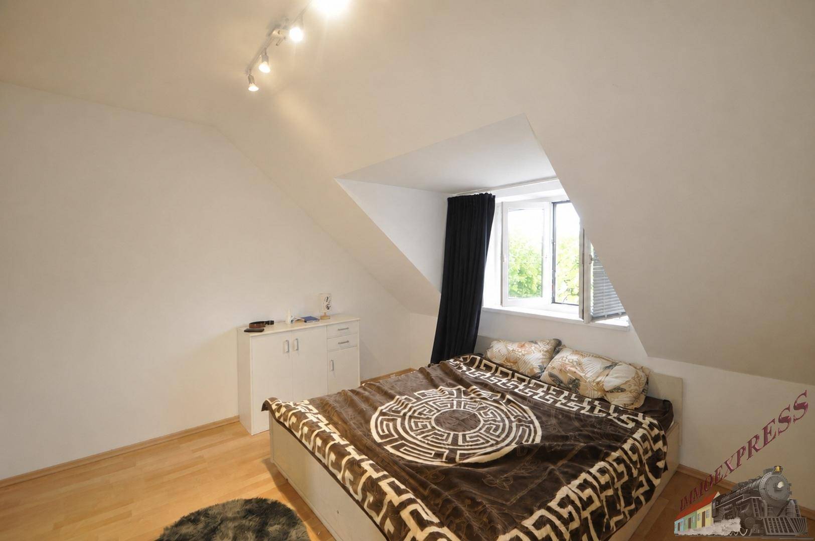Gemütliches Schlafzimmer mit Doppelbett, Holzboden und einem Fenster unter der Dachschräge.