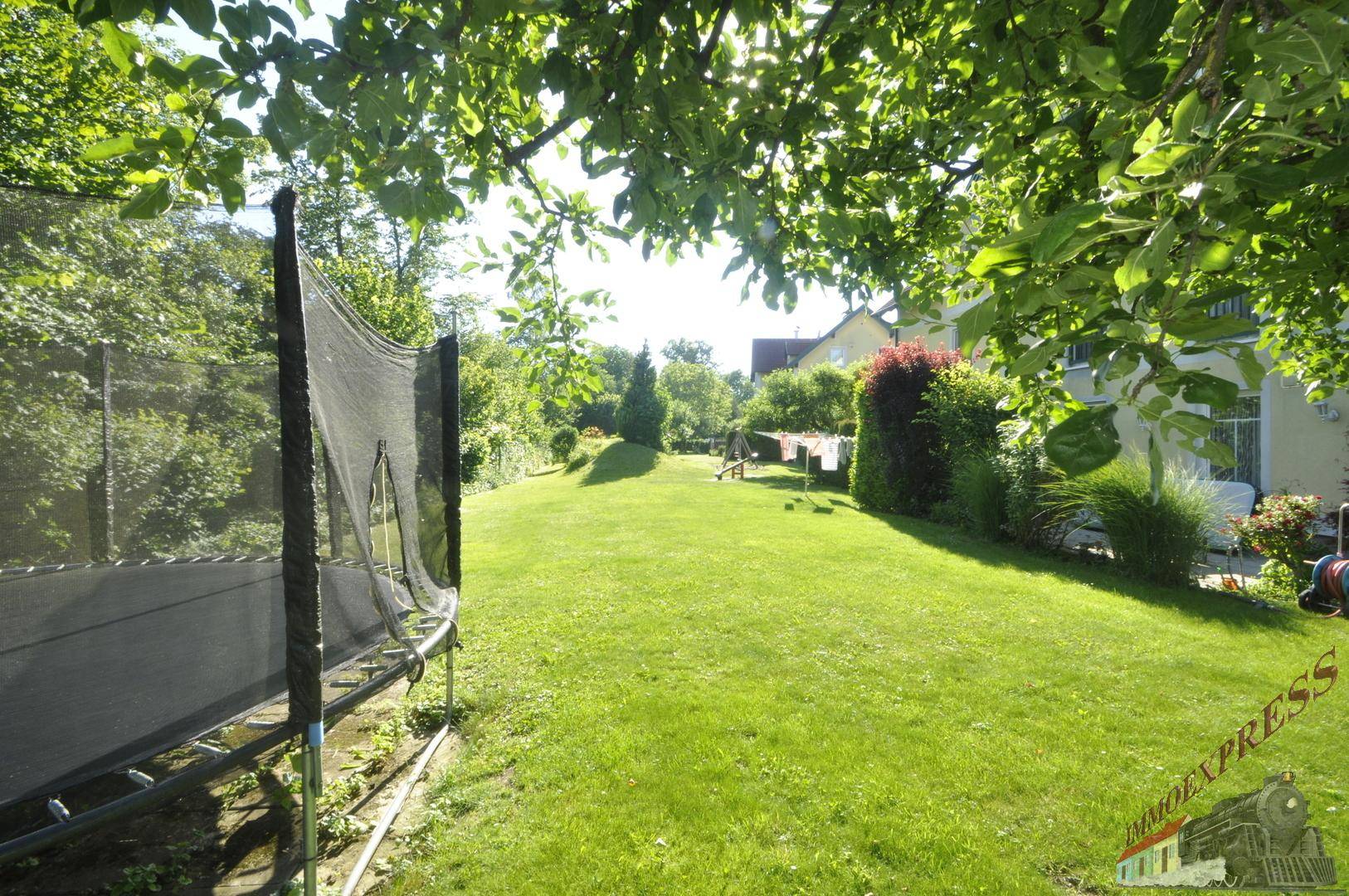 Weitläufiger Garten mit Rasenfläche, Trampolin und altem Baumbestand, ideal für Familien.