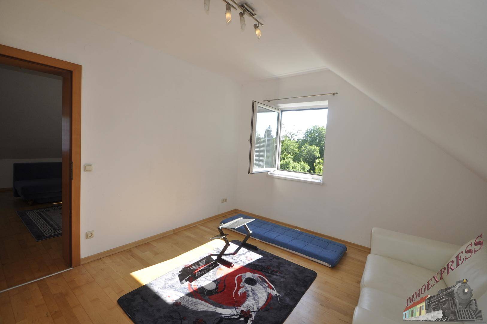 Helles Zimmer im Dachgeschoss mit Holzboden, Fenster und Blick ins Grüne.