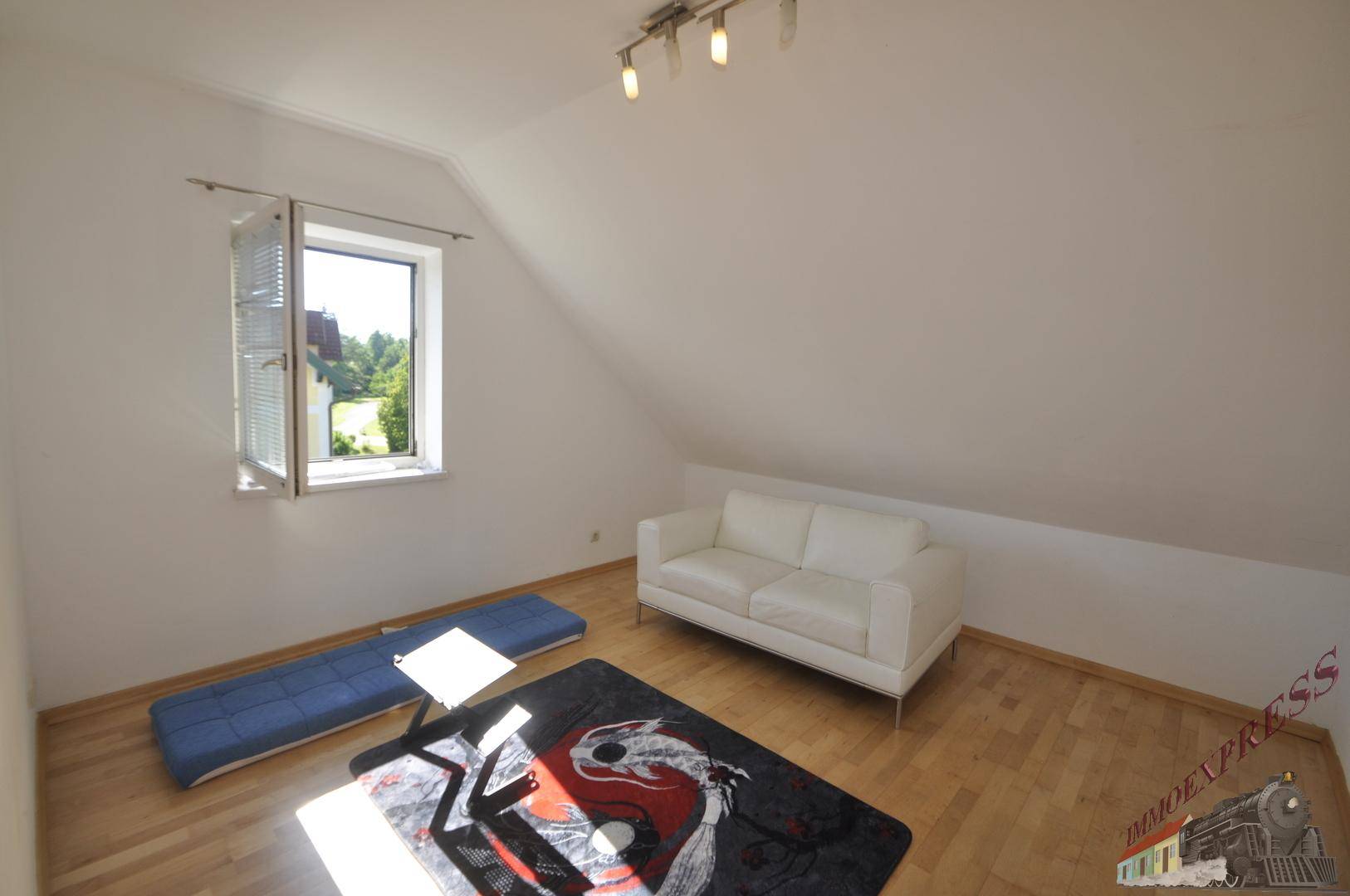 Freundliches Zimmer mit weißem Sofa, Holzboden und Dachschrägen, ideal als Gästezimmer.
