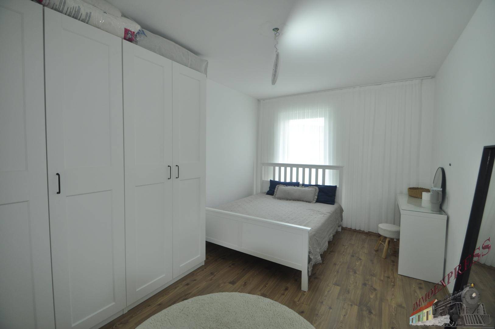 Helles Schlafzimmer mit weißem Bett, Kleiderschrank und Holzboden.