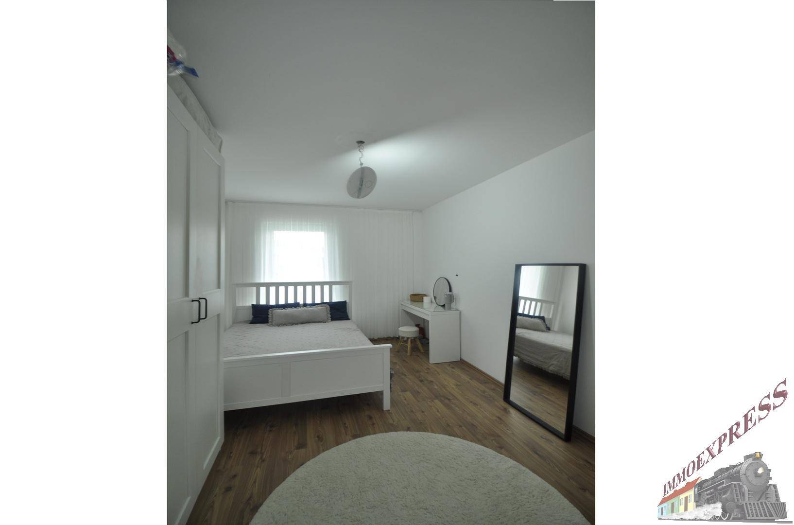 Schlafzimmer mit viel Tageslicht, Holzboden und einem großen Spiegel.