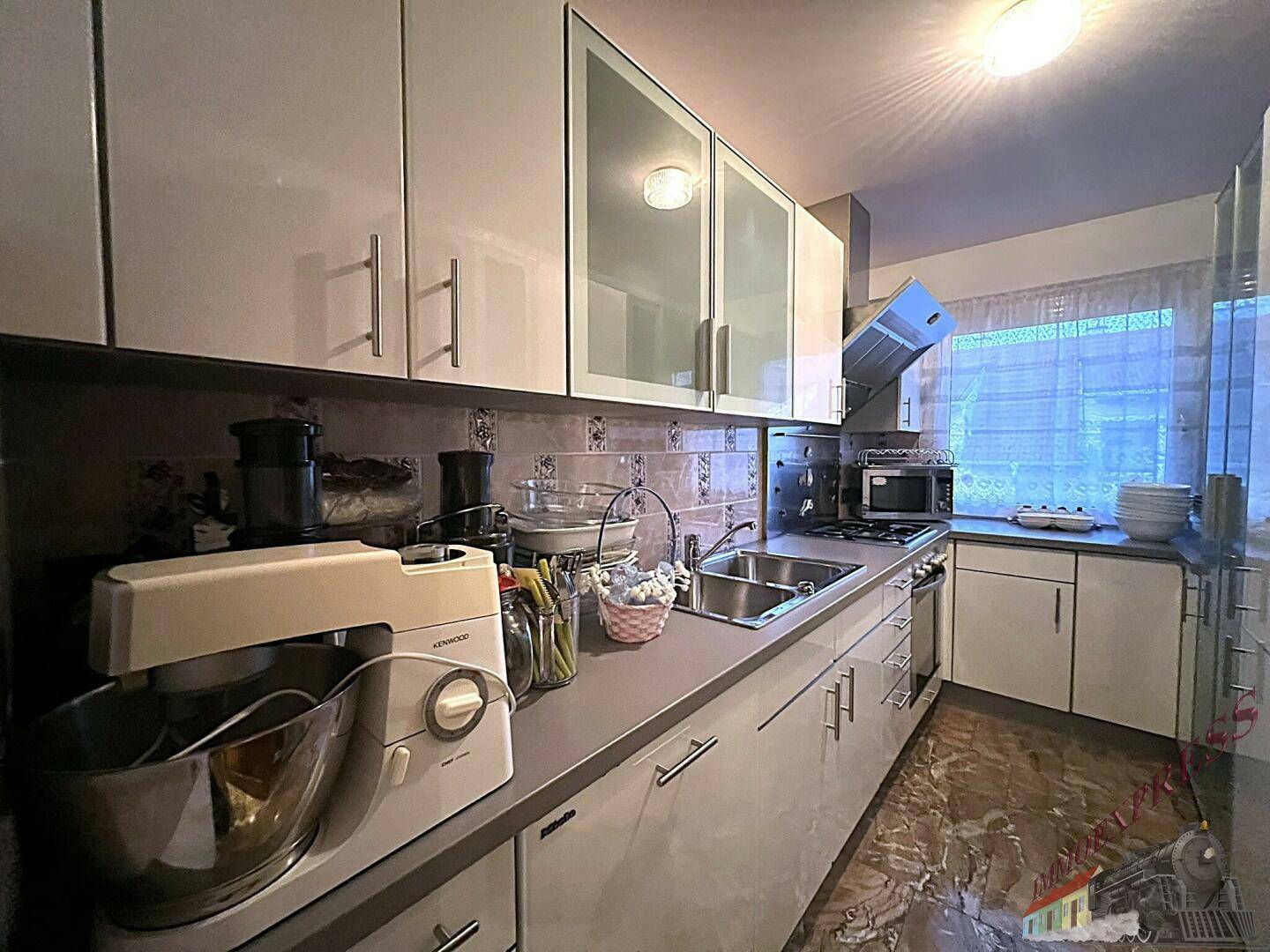 Moderne Küche mit weißen Hochglanzschränken, integrierten Geräten und einem großen Fenster.