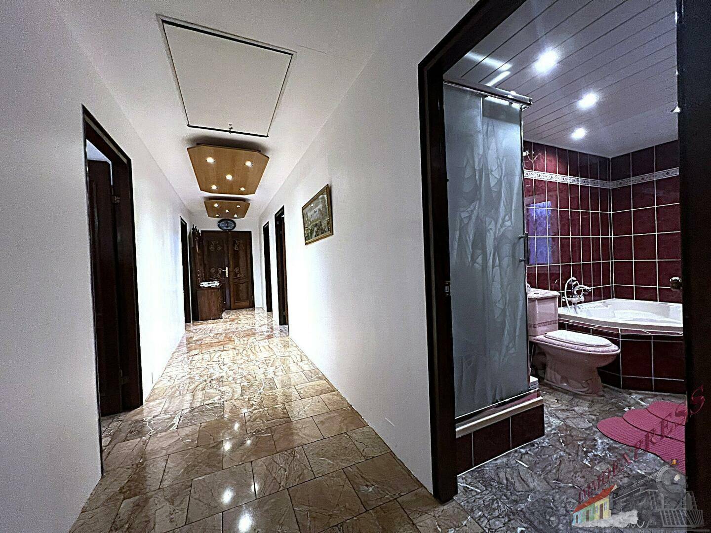 Langer Flur mit gefliestem Boden und Zugang zu einem Badezimmer mit Badewanne.