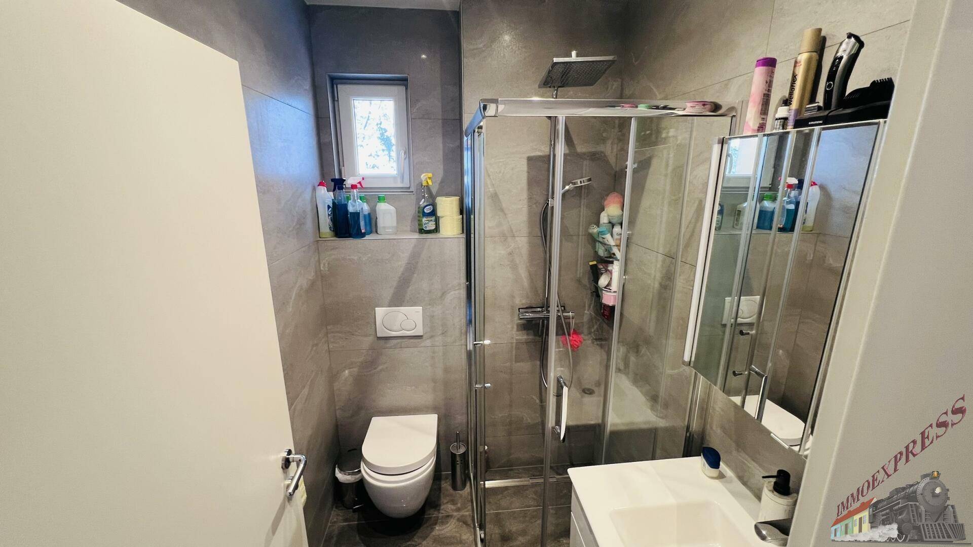 Modernes Badezimmer mit grauen Fliesen, wandhängendem WC und Duschkabine.