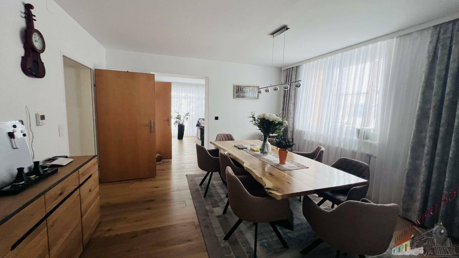 Heller Essbereich mit Holztisch und Parkettboden, der zu weiteren Räumen führt.