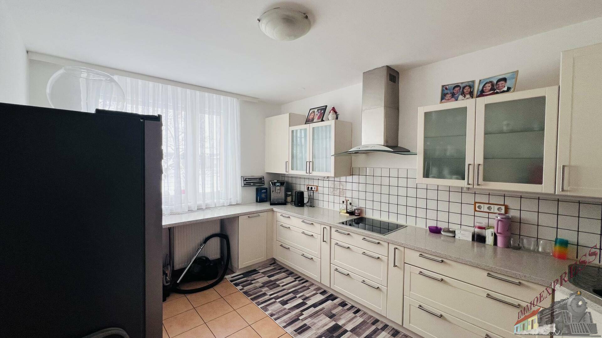 Helle Küche mit weißen Schränken, großem Fenster und Fliesenboden.