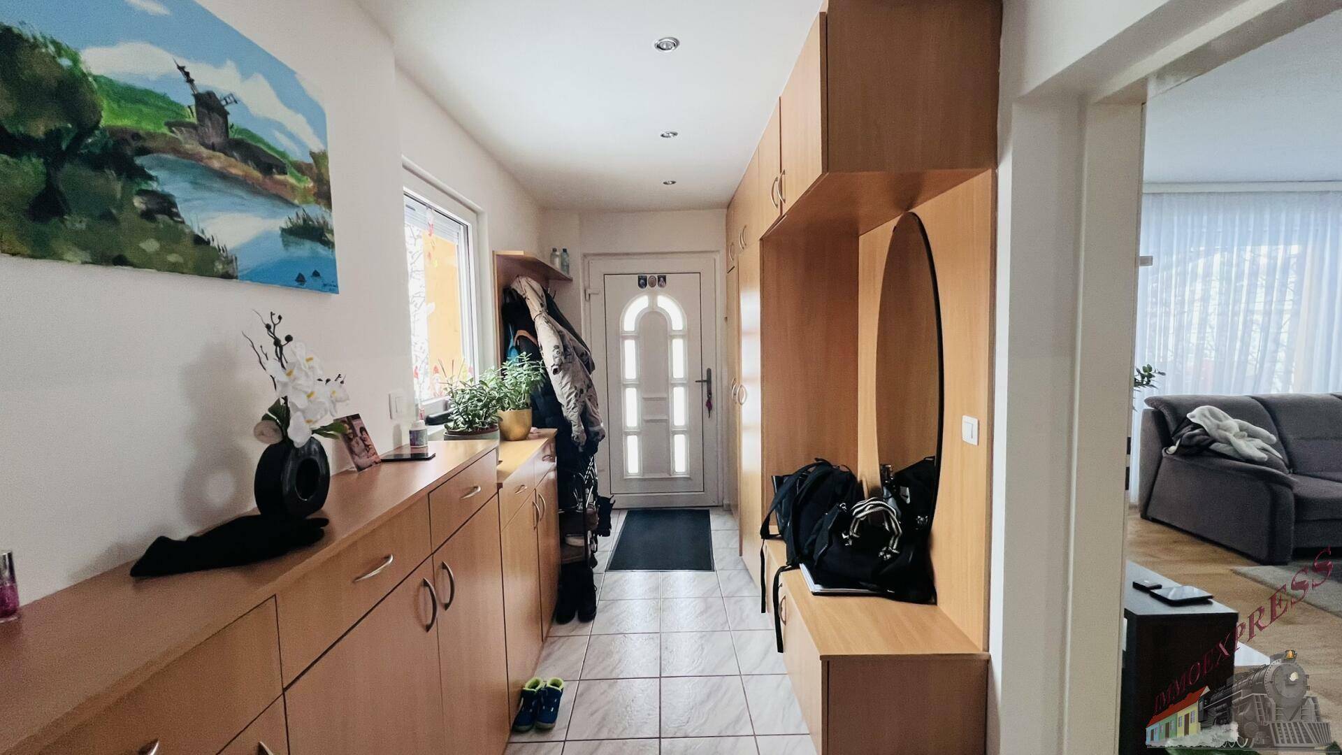 Heller Eingangsbereich mit Fliesenboden, Holzmöbeln und Garderobe, die zum Wohnbereich führt.