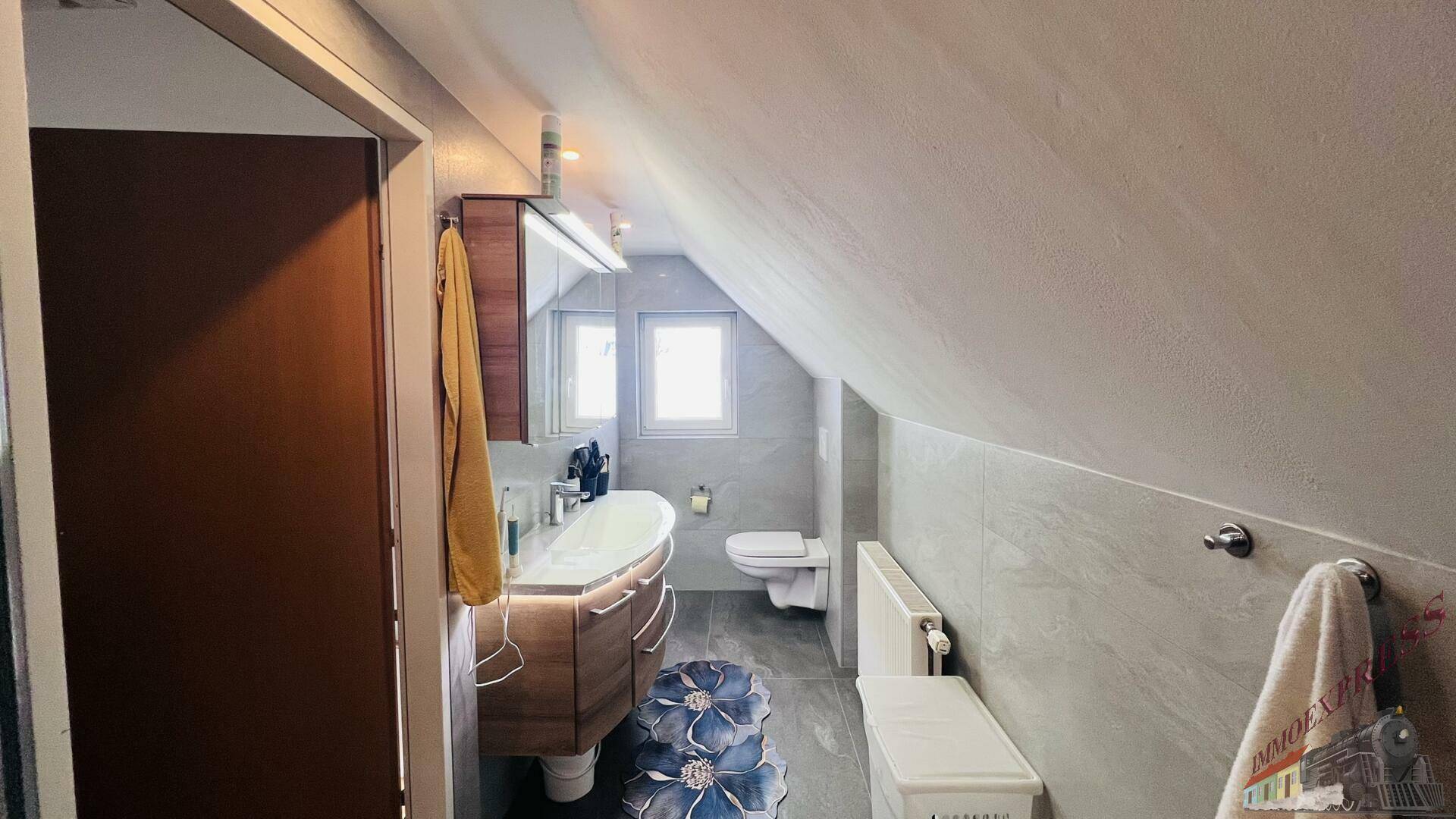 Modernes Badezimmer im Dachgeschoss mit Waschtisch, WC und schrägen Wänden.