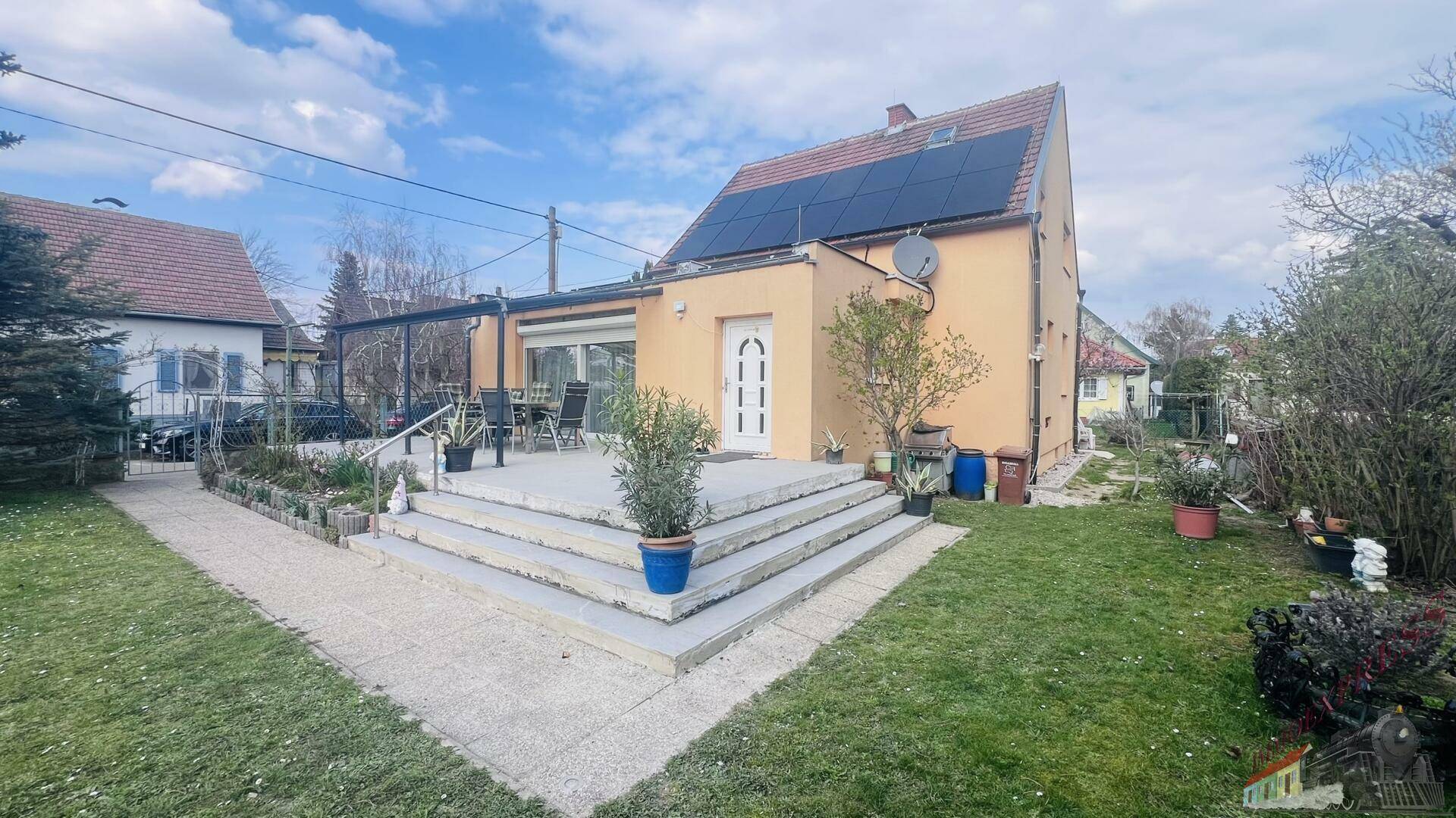 Gartenbereich mit Rasenfläche, gepflasterter Terrasse und dem Haus mit Photovoltaikanlage.