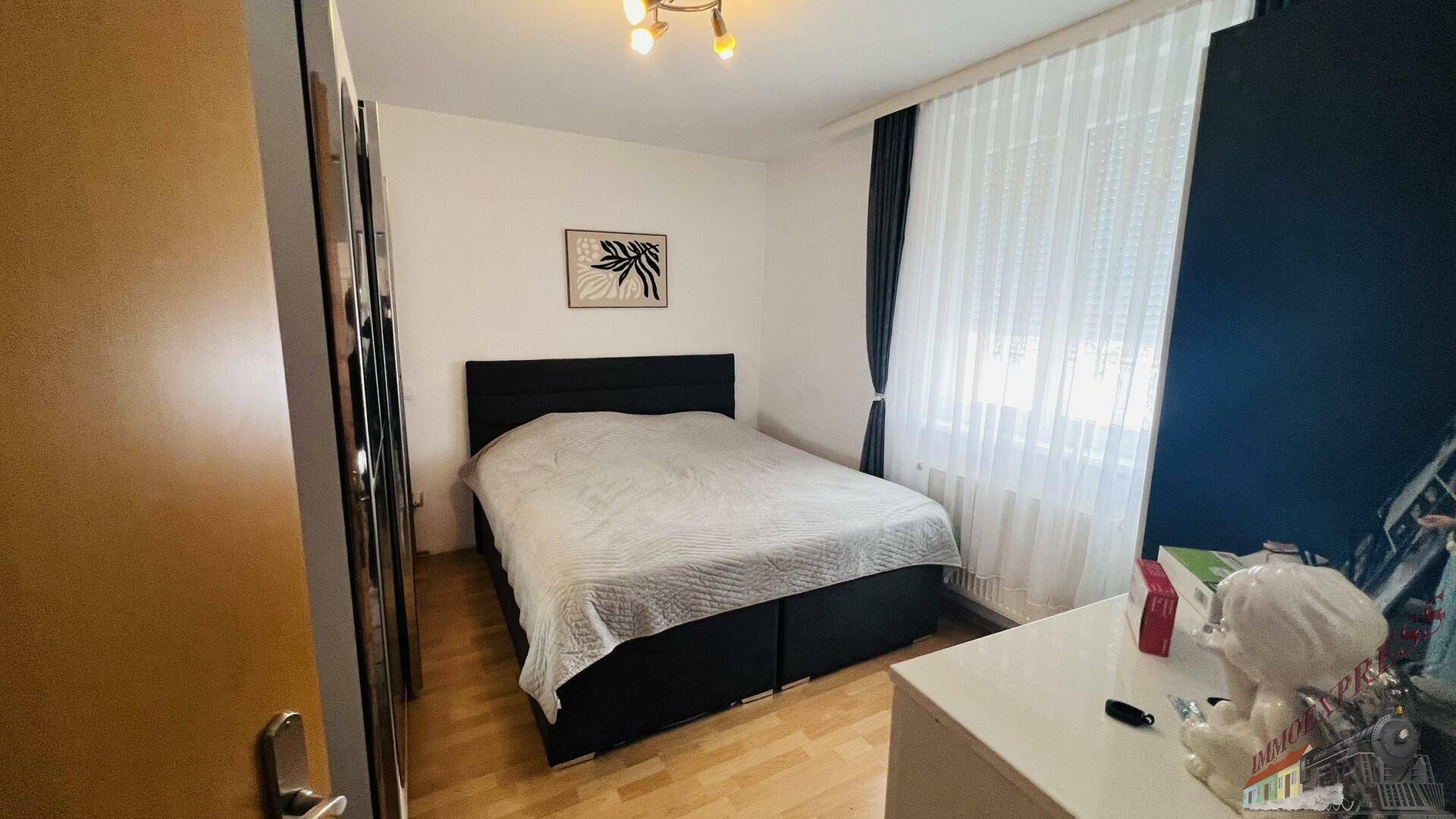 Helles Schlafzimmer mit Doppelbett, Holzboden und großem Fenster.