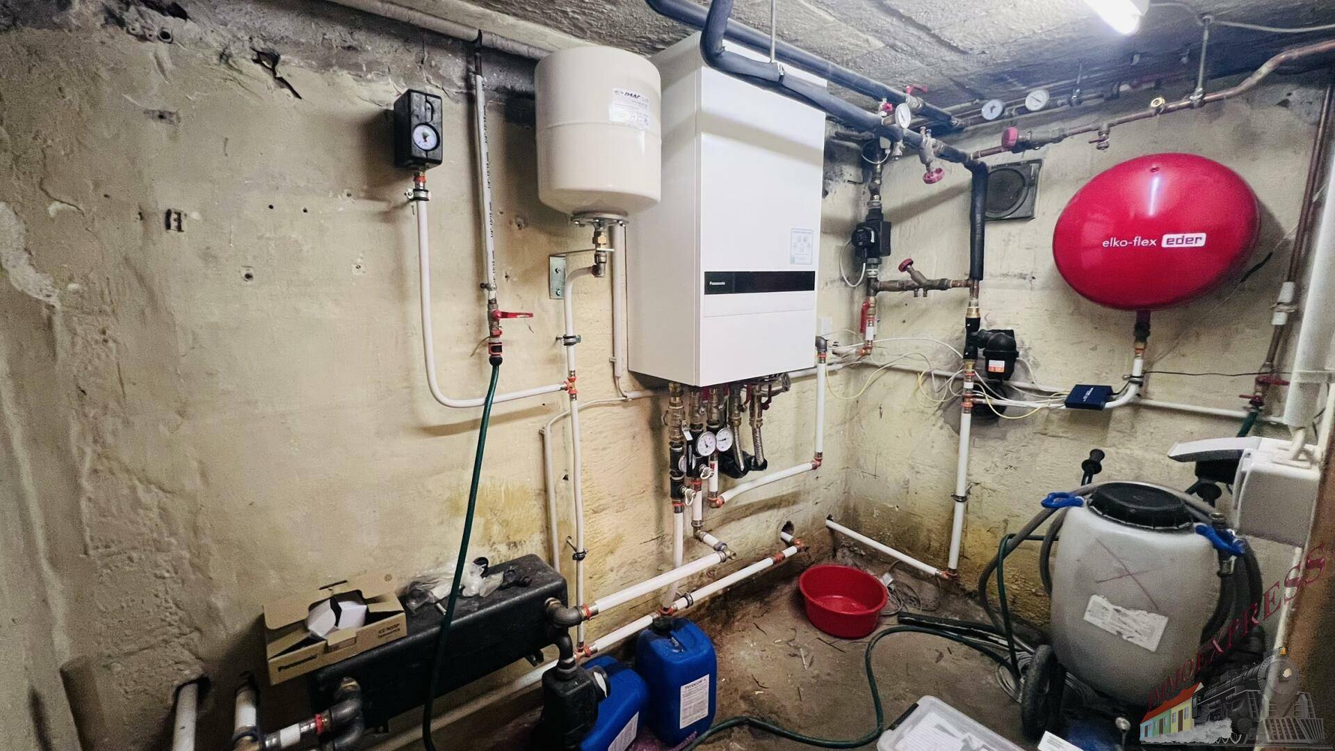 Technikraum im Keller mit Heizungsanlage, Warmwasserspeicher und Rohren.