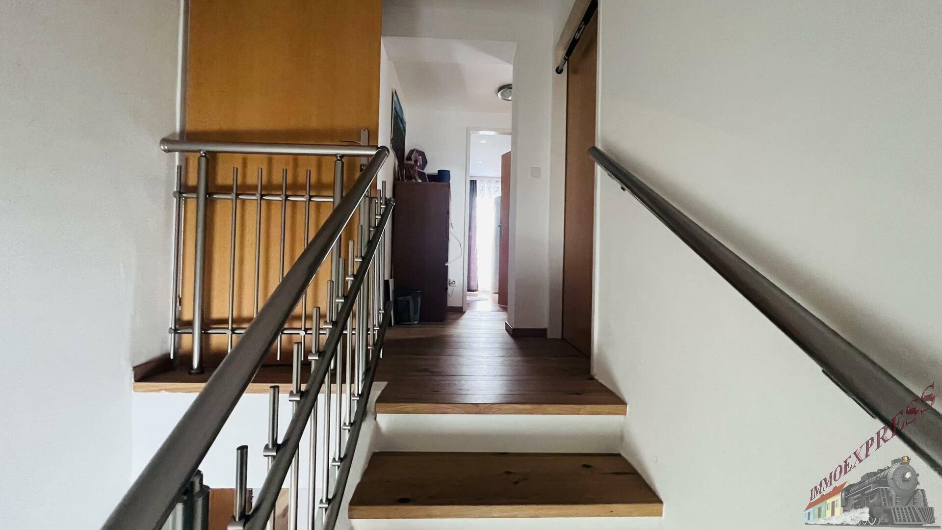 Treppenhaus mit Holzstufen und Edelstahlgeländer, das zu den oberen Etagen führt.