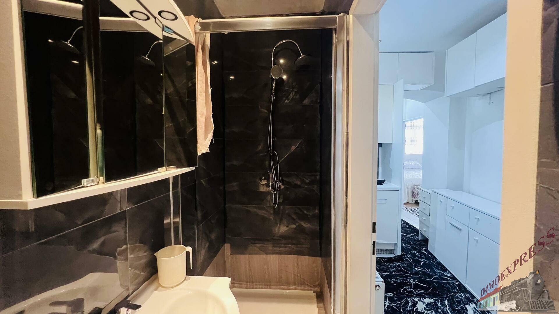 Modernes Badezimmer mit Duschkabine, Waschbecken und Spiegelschrank, ausgestattet mit dunklen Fliesen.