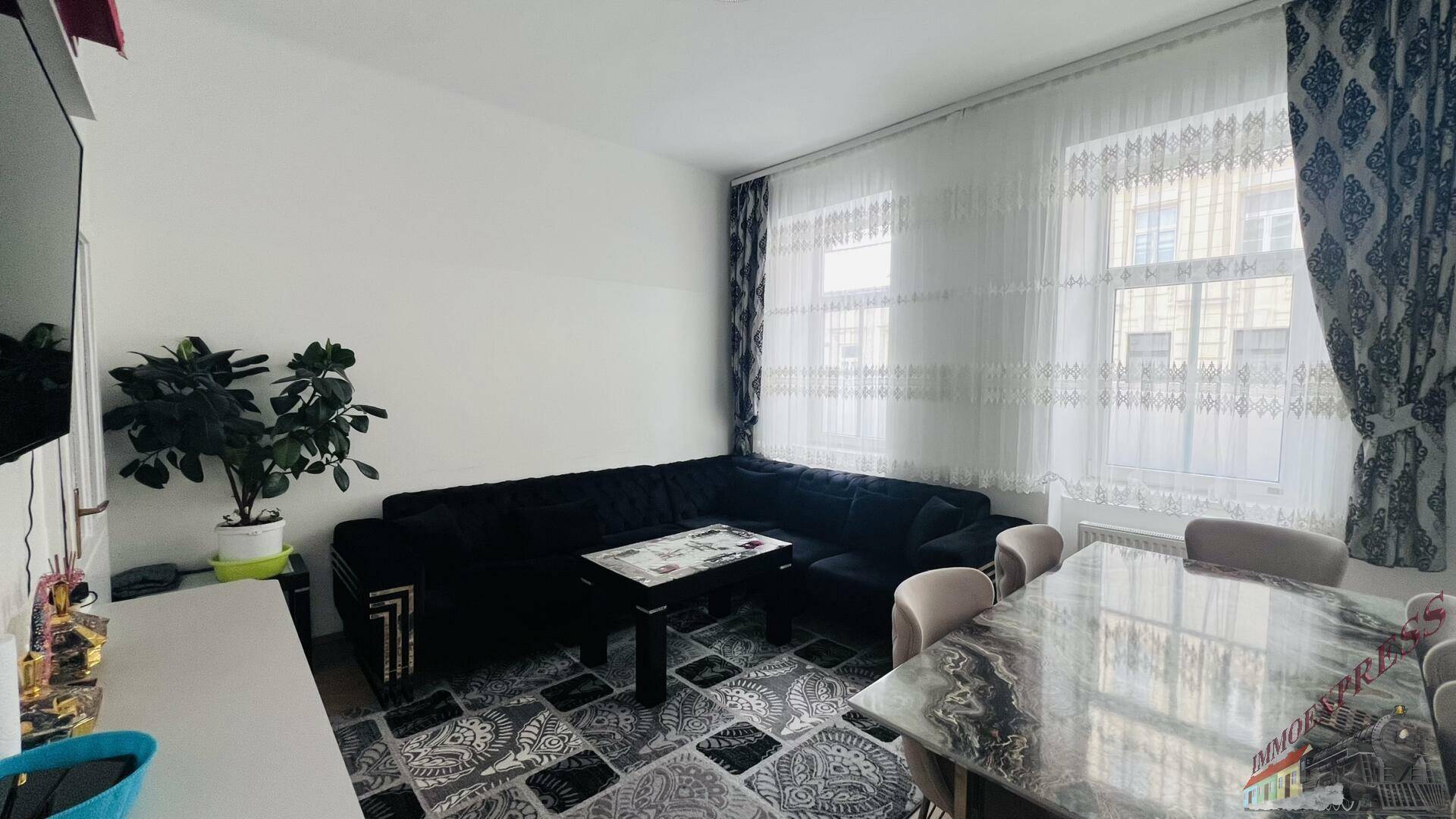 Gemütlicher Wohnbereich mit schwarzem Ecksofa, Couchtisch und einem Essbereich am Fenster.
