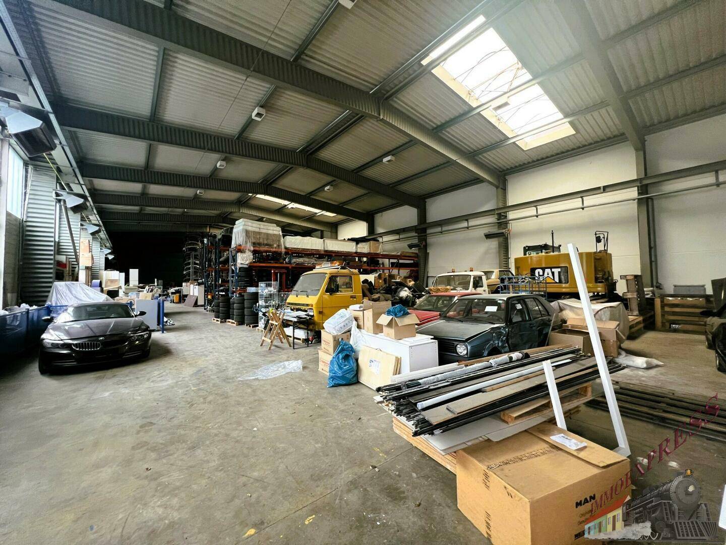 Geräumige Lagerhalle mit hohen Decken, Regalen und verschiedenen Fahrzeugen und Materialien, gut beleuchtet.