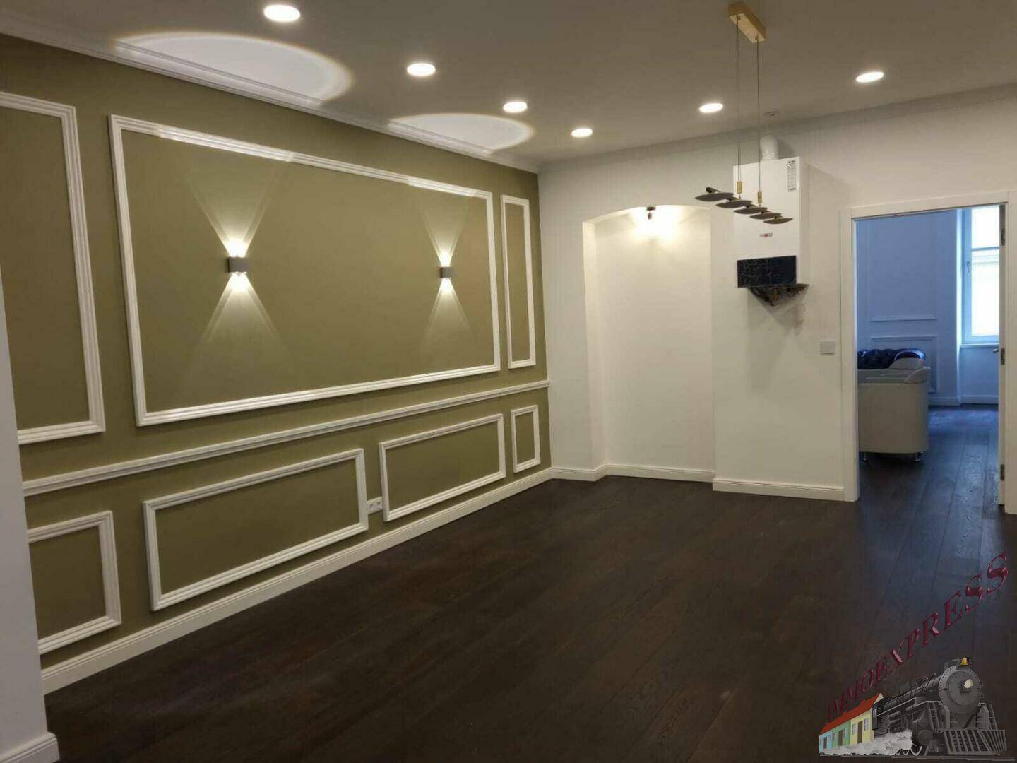 Leeres Wohnzimmer mit dunklem Holzboden, dekorativen Wandleisten und moderner Deckenbeleuchtung.