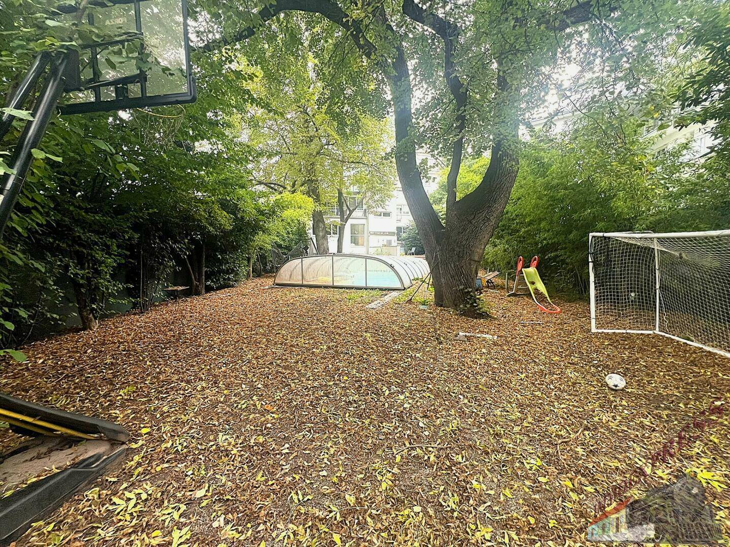 Großer Garten mit überdachtem Pool, Basketballkorb und Fußballtor, umgeben von Bäumen und Laub.