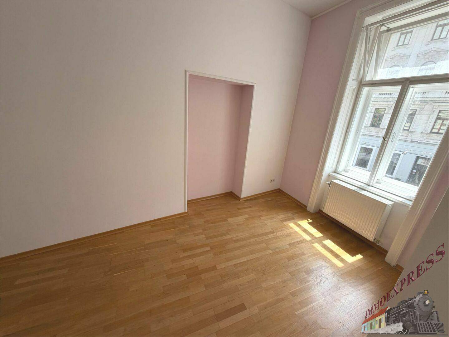 Heller Raum mit Holzboden, Wänden in Weiß und Rosa, einer Nische und einem Fenster.