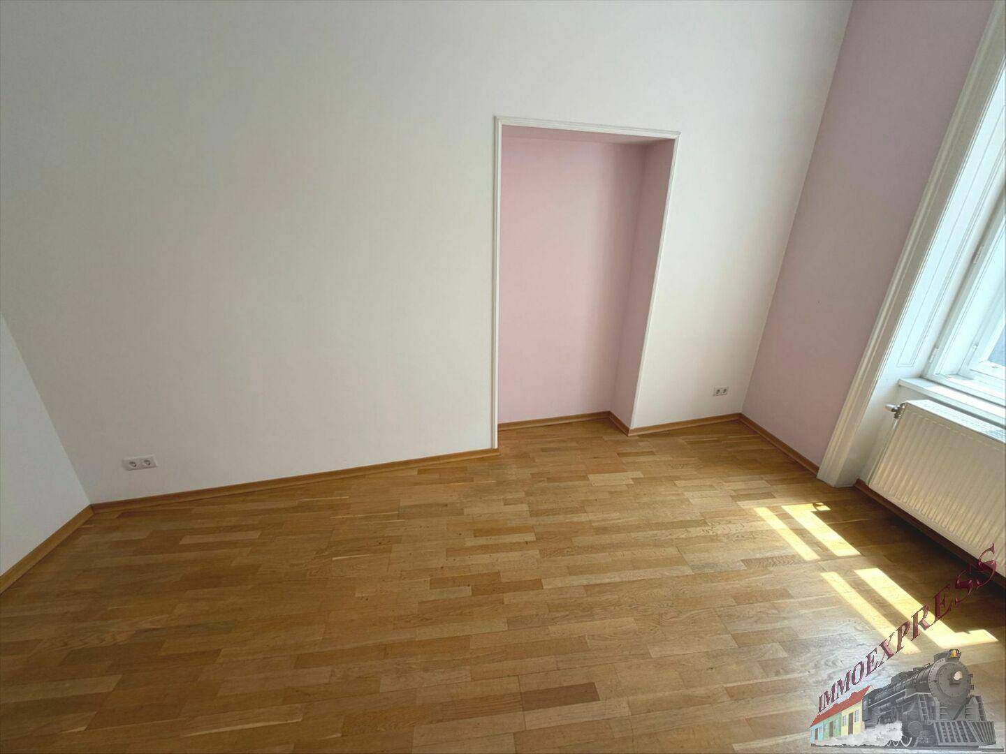 Gemütlicher Raum mit Holzboden, hellen Wänden, einer Nische und einem Fenster mit Dachschräge.