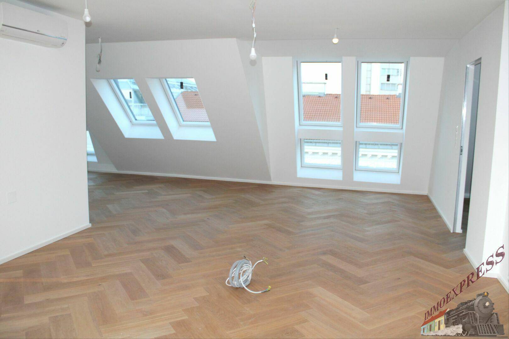 Geräumiges Dachgeschosszimmer mit Fischgrätparkett, Dachfenstern und Klimaanlage.