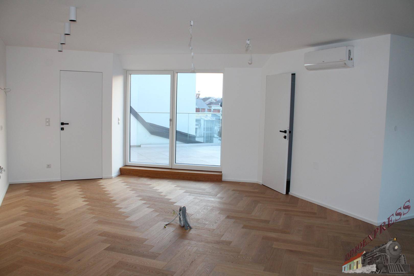 Geräumiger Wohnbereich mit Fischgrätparkett, Klimaanlage und Zugang zur Dachterrasse.