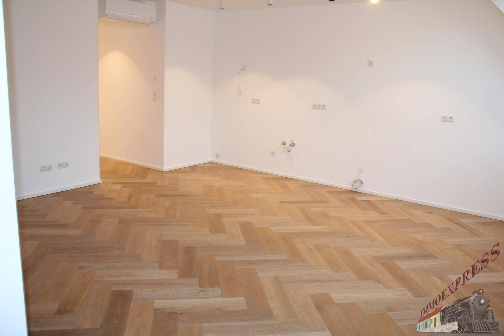 Heller Raum mit Fischgrätparkett und vorbereiteten Anschlüssen für die Installation.