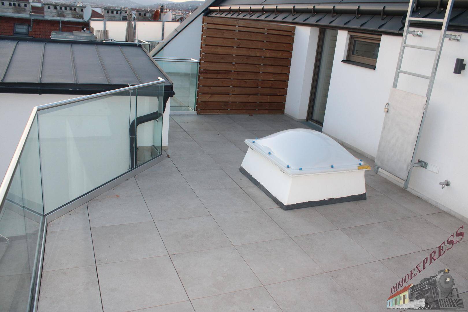 Geräumige Dachterrasse mit Glasgeländer, Fliesenboden und Dachfenster.