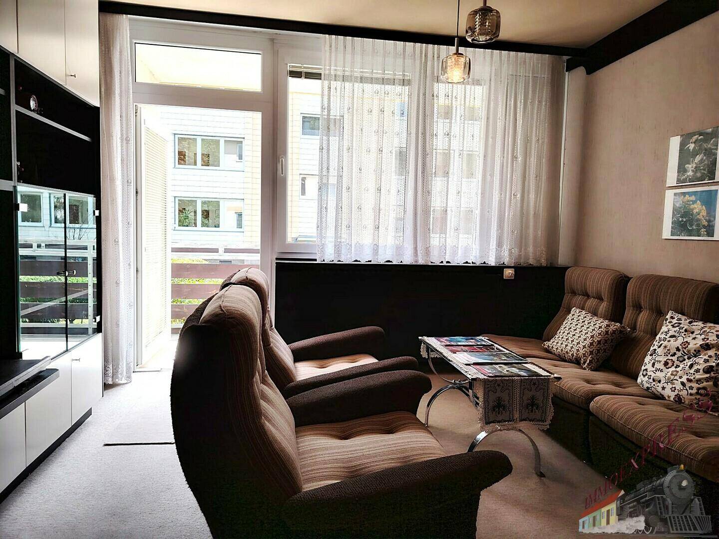 Helles Wohnzimmer mit Zugang zum Balkon, bequemen Sofas und Vorhängen.