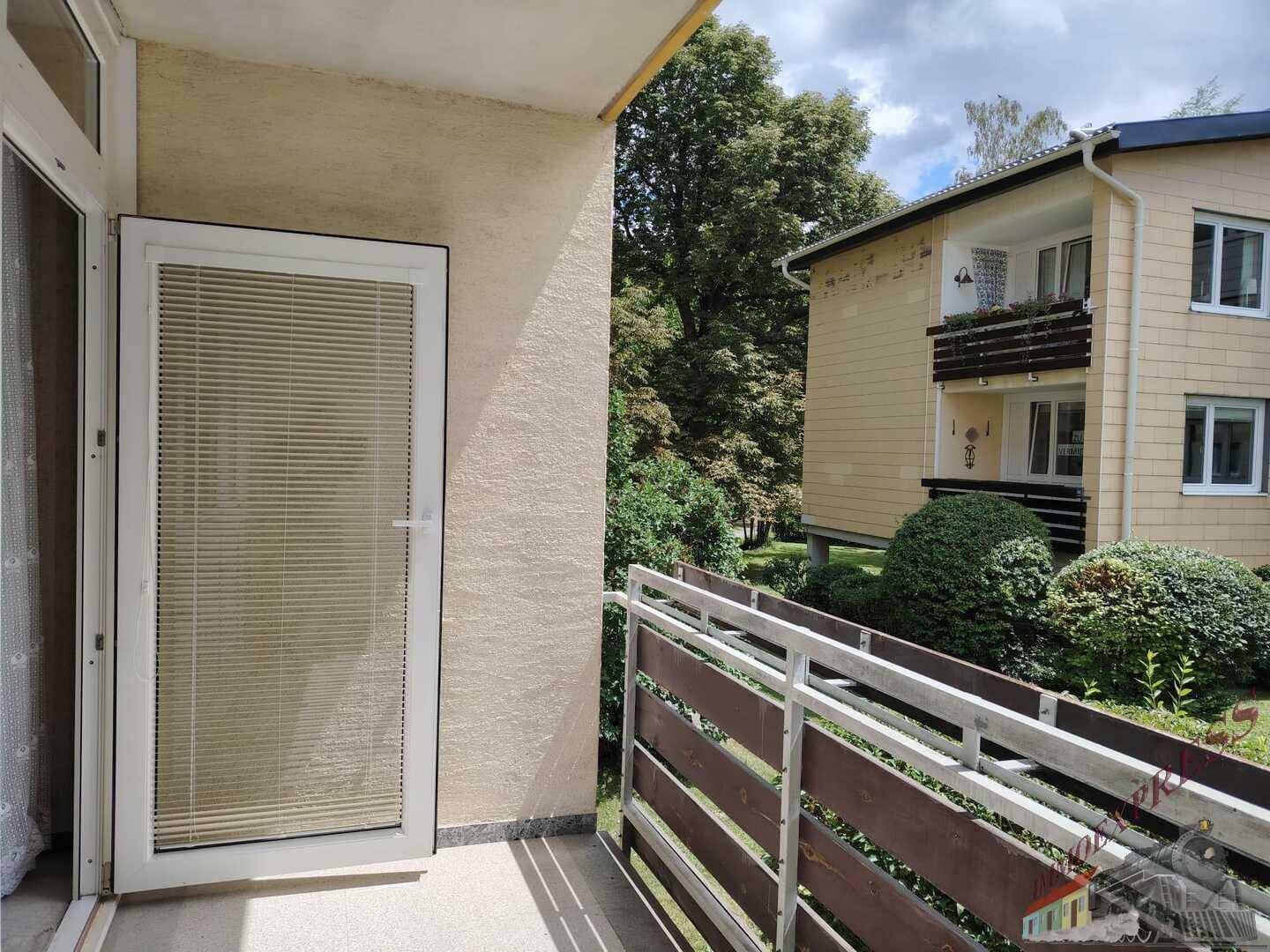 Balkon mit Rampe und Blick auf grüne Umgebung und benachbarte Gebäude.