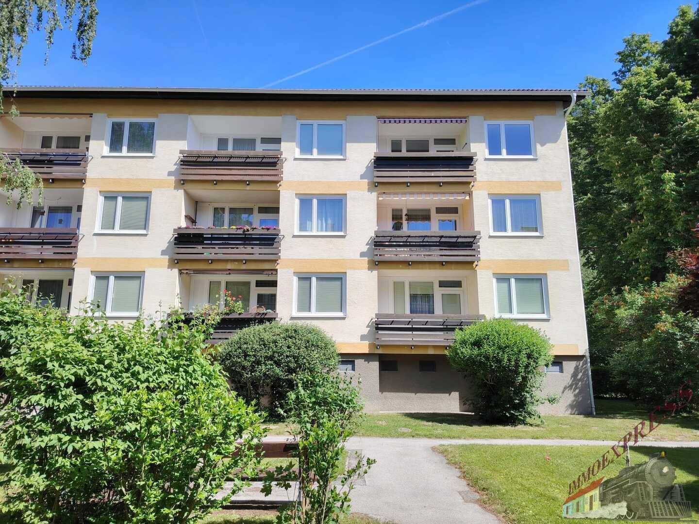 Mehrfamilienhausfassade mit mehreren Balkonen und umgebender Grünfläche.