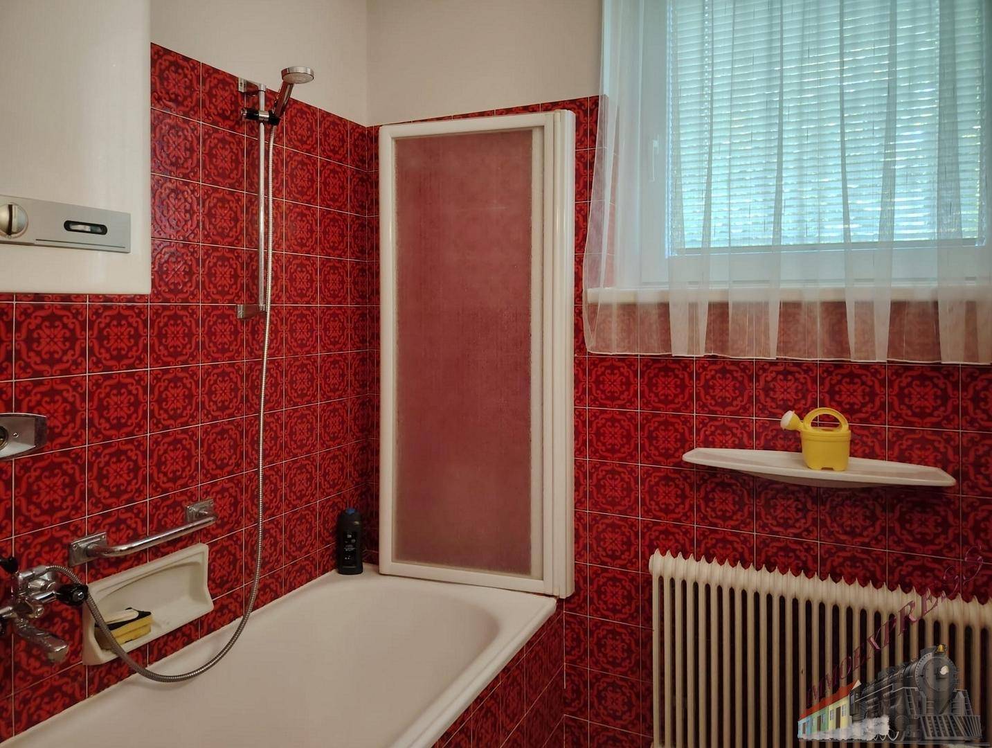 Badezimmer mit roten gemusterten Fliesen, Badewanne und Fenster für Tageslicht.