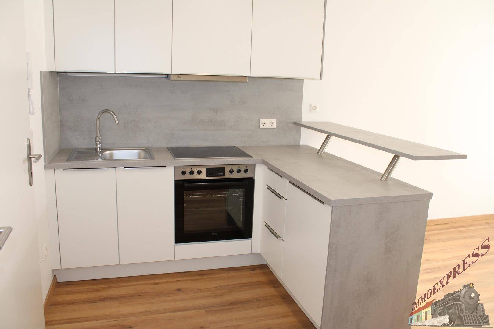 Moderne Einbauküche mit weißen Schränken, grauer Arbeitsplatte und integrierten Geräten.