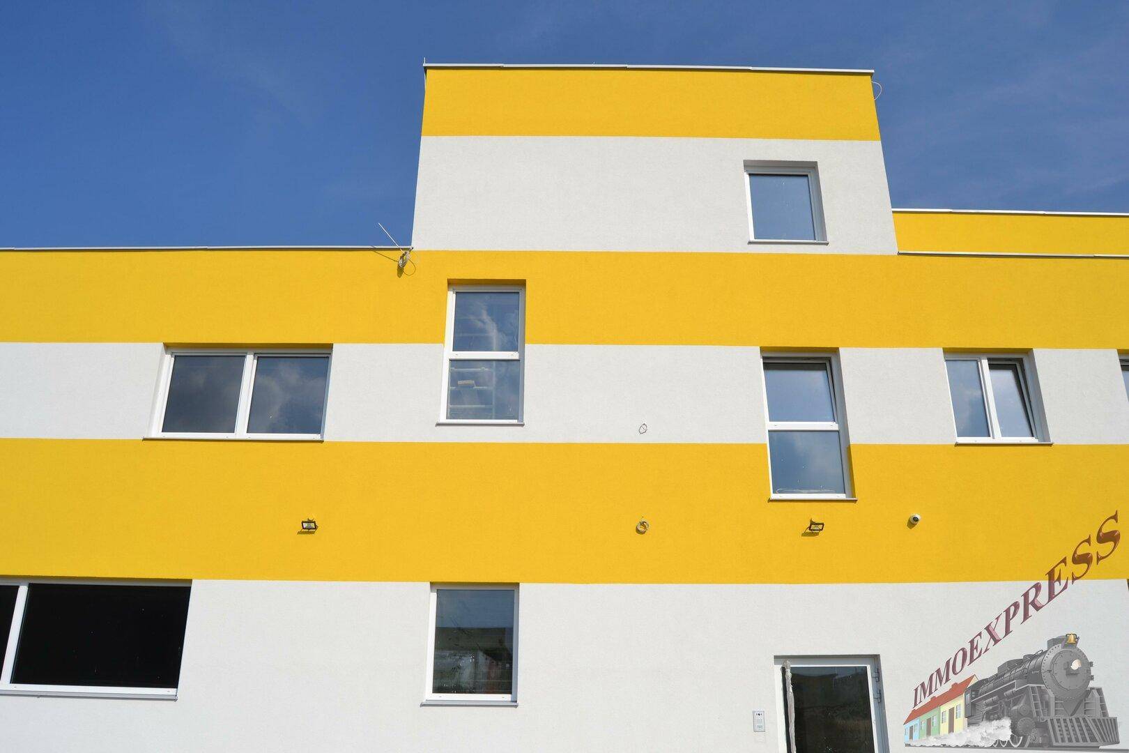 Moderne Gebäudefassade mit gelben und weißen Streifen sowie mehreren Fenstern.