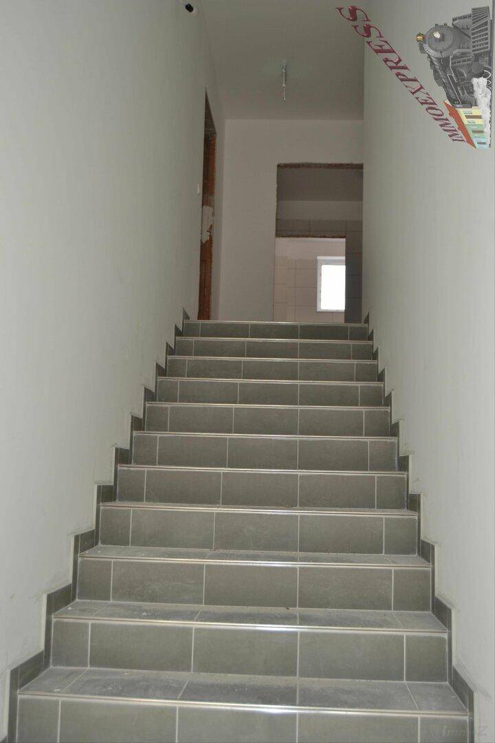 Geflieste Treppe mit grauen Fliesen, die nach oben führt, in einem hellen Treppenhaus.